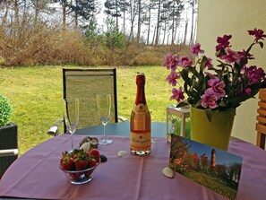 An outdoor table set with a bottle of wine, a glass, a bowl of strawberries, and a flower arrangement. - Right on the beach, upscale amenities, 25 meters to the sandy beach, Wi-Fi (Juliusruh)