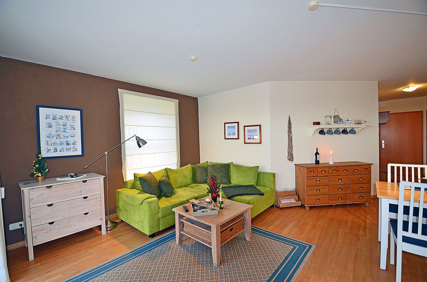 Een woonkamer met een groene bank, een houten dressoir, een klein tafeltje met een kaars en een blauw tapijt met dessin.