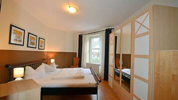 A hotel room with a bed, bedside lamps, a window with curtains, a wardrobe with mirrored doors, and framed pictures on the wall.