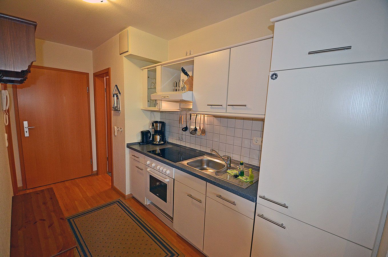 Een kleine keuken met een fornuis, spoelbak en witte keukenkastjes.