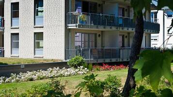 A multi-story residential building with balconies, a landscaped garden, and a clear sky.