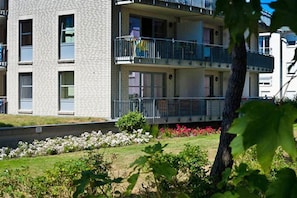 Ein mehrstöckiges Wohngebäude mit Balkonen, einem angelegten Garten und blauem Himmel.