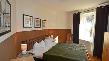 A hotel room with a bed, bedside lamps, a chair, a window with curtains, and framed pictures on the wall.