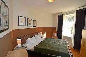 Ein Hotelzimmer mit einem Bett, Nachttischlampen, einem Sessel, einem Fenster mit Vorhängen und gerahmten Bildern an der Wand.