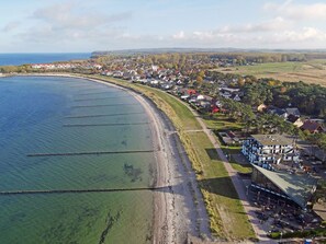 Eine Vogelperspektive einer Küstenstadt mit Strand, Häusern und einem großen Gebäude mit flachem Dach.