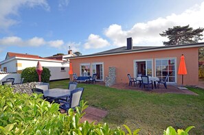 Ein Wohnhaus mit Terrasse, die Gartenmöbel und Sonnenschirme umfasst, einer Steinmauer und einem gepflegten Rasen.