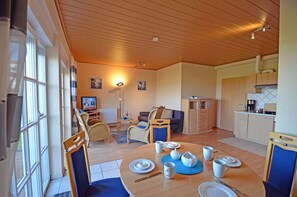 Ein gemütliches Wohnzimmer mit Esstisch für vier Personen, einer Küchenzeile und einem Fernseher im Hintergrund.