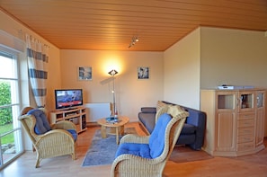 Ein Wohnzimmer mit Korbmöbeln, einem Fernseher, einem Tisch und einem Schrank.