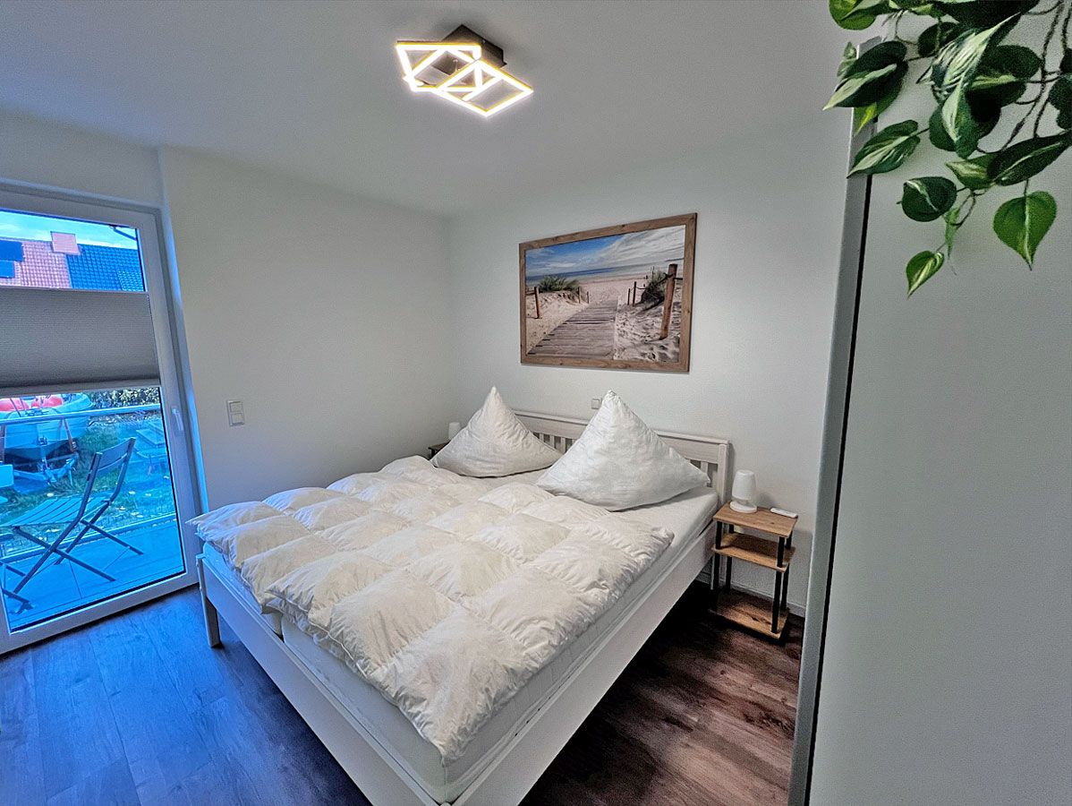 Un dormitorio con una cama, una mesita de noche, un cuadro en la pared y vistas por una ventana.