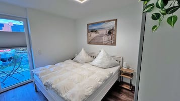 Un dormitorio con una cama, una mesita de noche, un cuadro en la pared y vistas por una ventana.