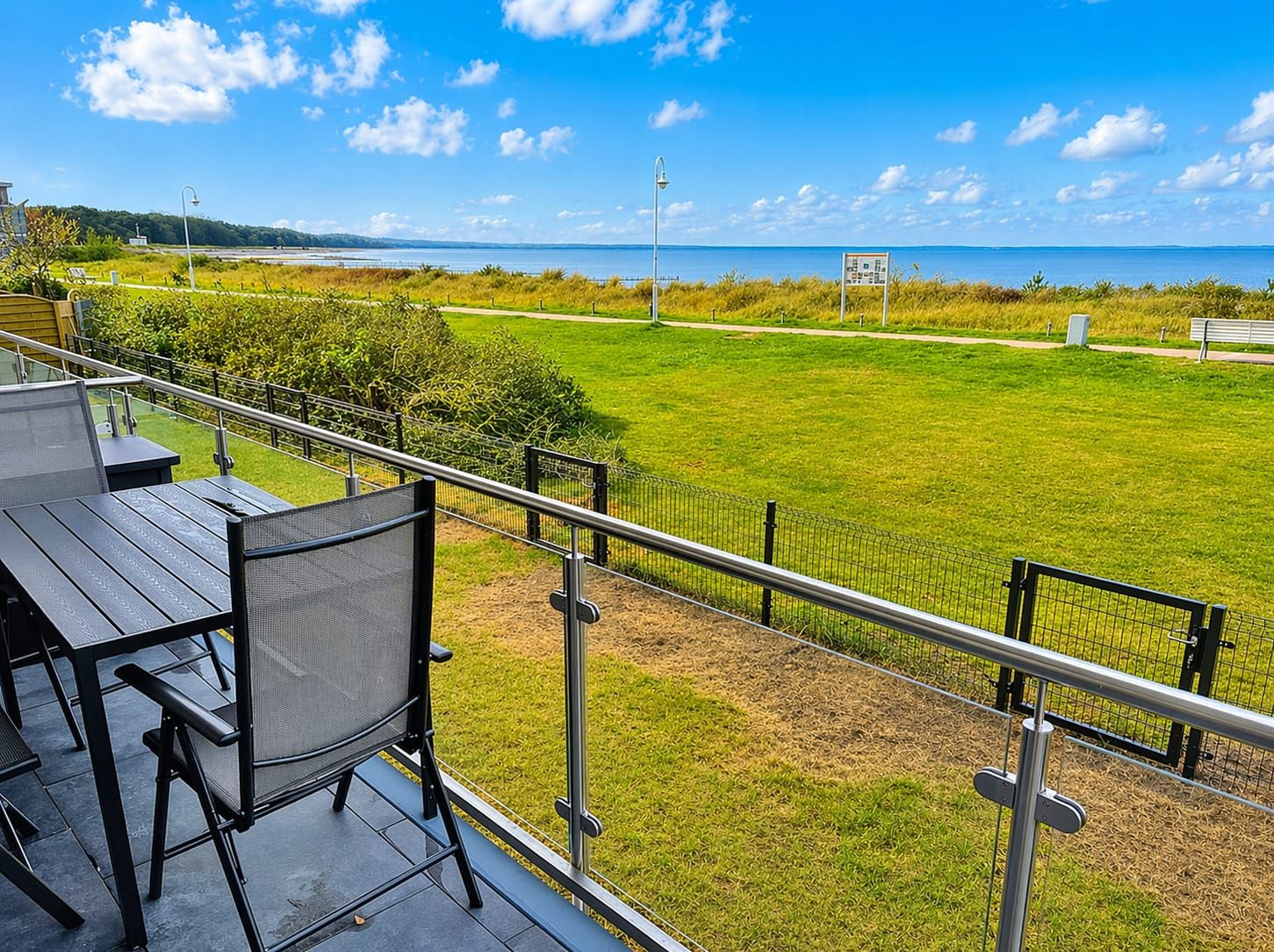 A balcony with outdoor seating overlooking a grassy area and a body of water.