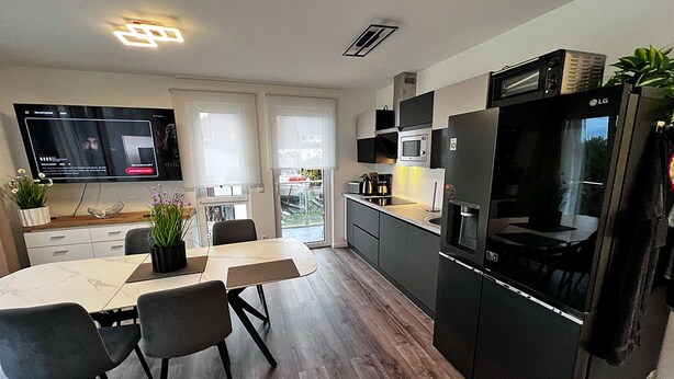Una cocina moderna con comedor, electrodomésticos integrados y un televisor de pantalla plana.