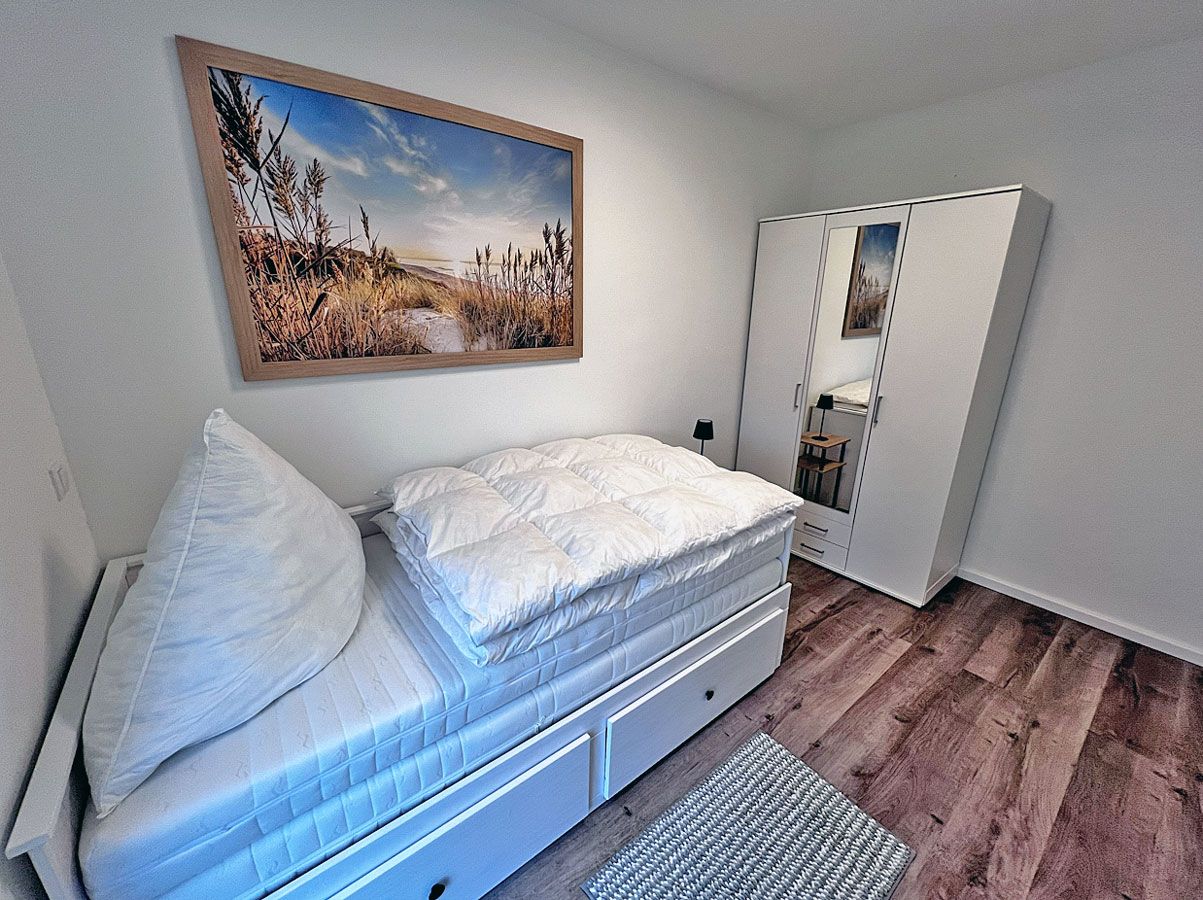 A bedroom with a bed, a nightstand, a wardrobe, and a painting on the wall.