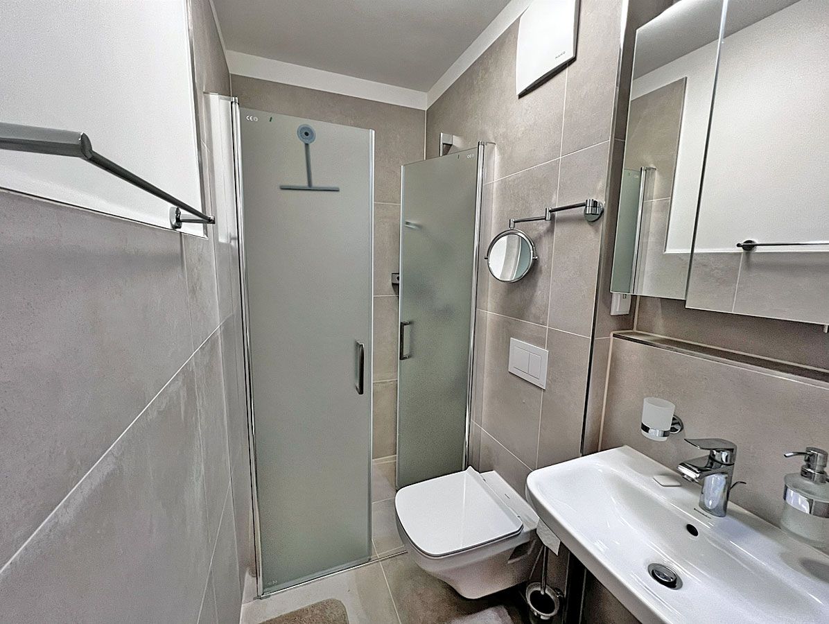 Een moderne badkamer met een glazen douchecabine, een wit toilet en een wastafel met spiegel.