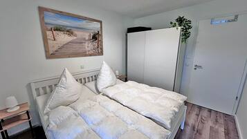 A bedroom with a bed, a bedside table, a nightstand, a wardrobe, and a door.