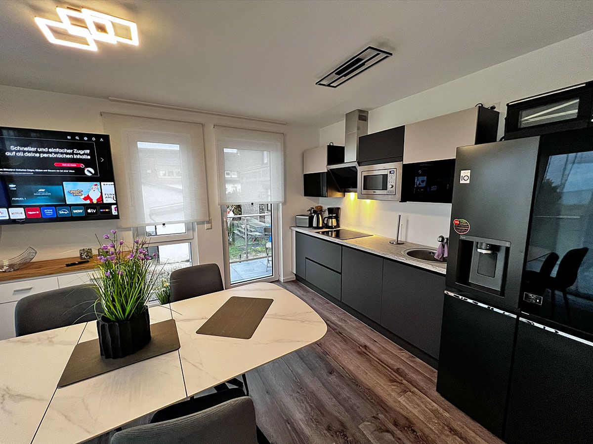 A modern kitchen with a dining area, a flat-screen TV, and a refrigerator.