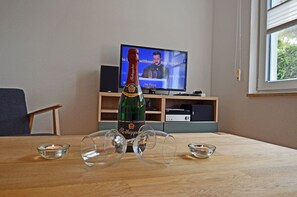 A room with a wooden table, a bottle of wine, glasses, a candle, and a television displaying a news channel. - Right on the Baltic Sea beach, upscale amenities, 30 m from the sandy beach, Wi-Fi (Juliusruh)