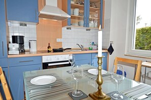 A modern kitchen with blue cabinets, a gas stove, and a dining table set for four with wine glasses and plates. - Right on the Baltic Sea beach, upscale amenities, 30 m from the sandy beach, Wi-Fi (Juliusruh)