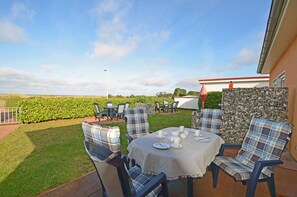 An outdoor patio with a table set for tea, surrounded by chairs with plaid cushions, a stone wall, and a view of the countryside. - Right on the Baltic Sea beach! Just 20 meters to the beach, patio, sleeps up to 4 people (Glowe)