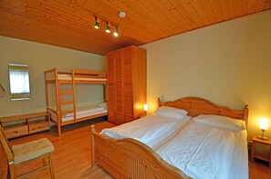 A room with a bunk bed, a single bed, a wooden wardrobe, a bedside table with a lamp, a wooden chair, and a small desk with drawers. - Right on the Baltic Sea beach! Just 20 meters to the beach, patio, sleeps up to 4 people (Glowe)