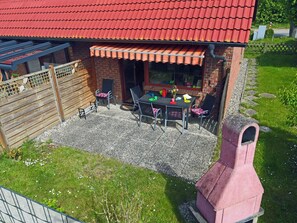 Eine Terrasse mit einem Grill aus Ziegelsteinen, einem Tisch mit Stühlen und einem Holzzaun.