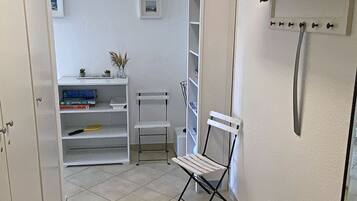 Ein Zimmer mit einem weißen Stuhl, einem Bücherregal, einem Kleiderhaken und einer Tür.