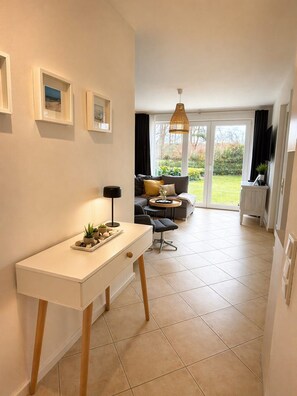 A modern living room with a sofa, a coffee table, and a dining area with a table and chairs. There is a large window providing a view of the outdoors. - Right on the beach with a terrace, upscale amenities, 30 m to the sandy beach, Wi-Fi, (Juliusruh)