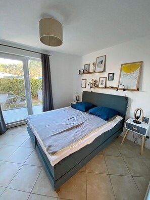Quarto com cama, mesa de cabeceira, abajur e vista pela porta de vidro deslizante.