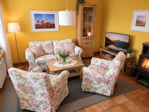 Ein gemütliches Wohnzimmer mit einer Couch, zwei Sesseln, einem Couchtisch, einem Fernseher und einem Kamin.