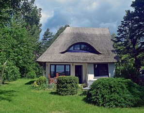 Uma casa com telhado de palha, varanda da frente e jardim.
