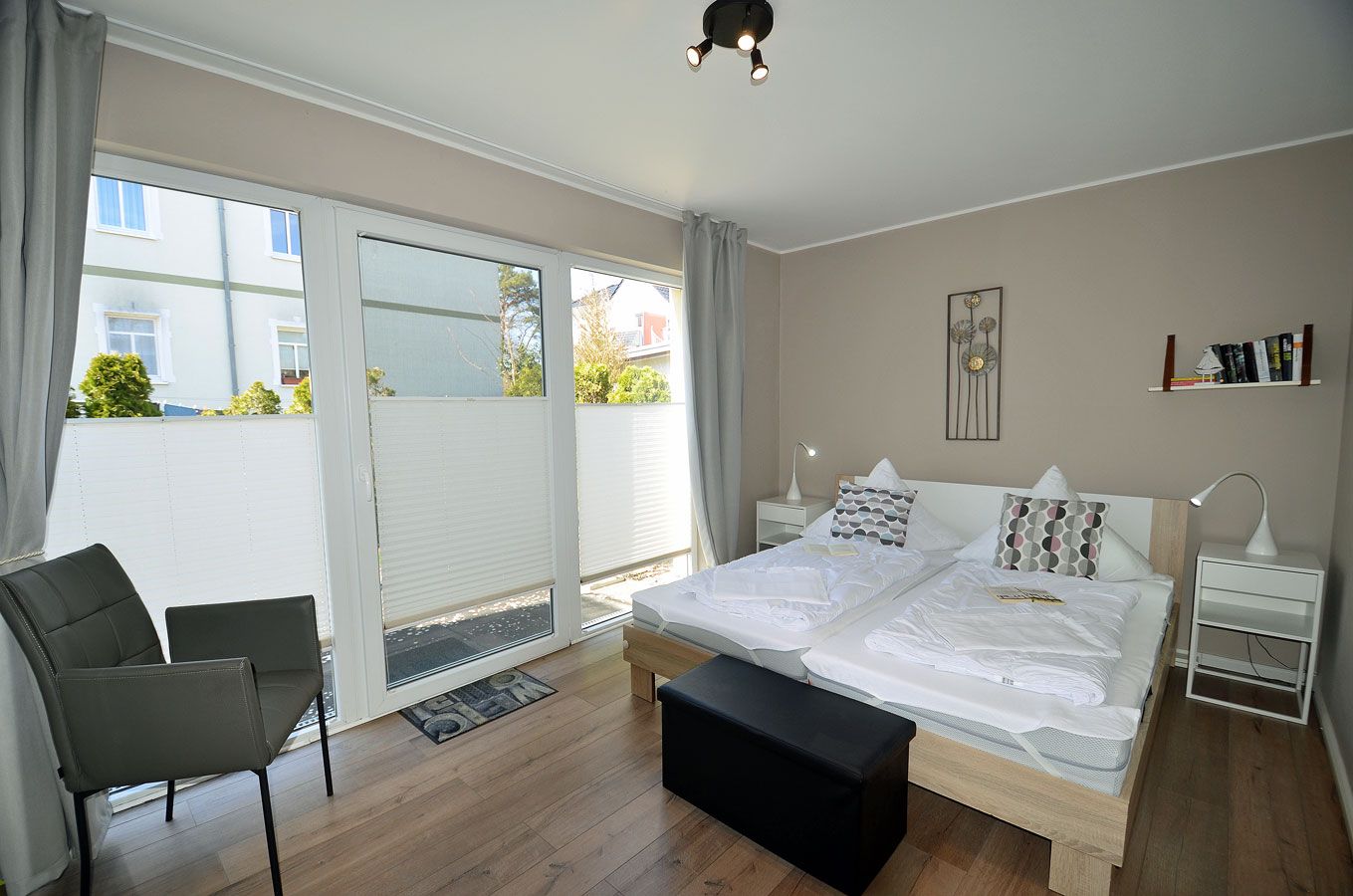 A bedroom with a large bed, a chair, a bedside table, a lamp, and a view through a sliding door to the outside.