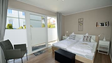 A bedroom with a large bed, a chair, a bedside table, a lamp, and a view through a sliding door to the outside.