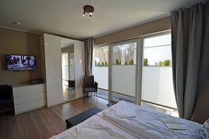 A hotel room with a bed, a desk, a chair, a television, and a sliding glass door to the outside. - First floor, modern amenities, central location, about 200 m from the sandy beach (Baltic Sea) (Juliusruh)