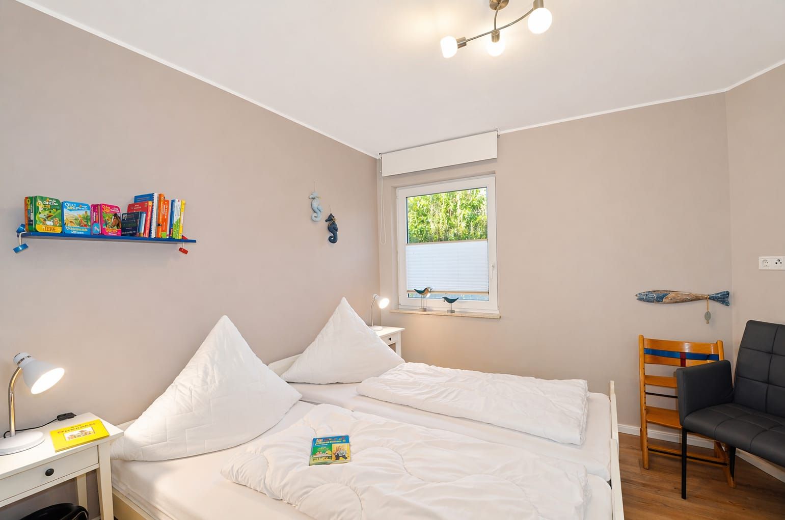 A bedroom with a bed, bedside table, lamp, bookshelf, window, and a chair.