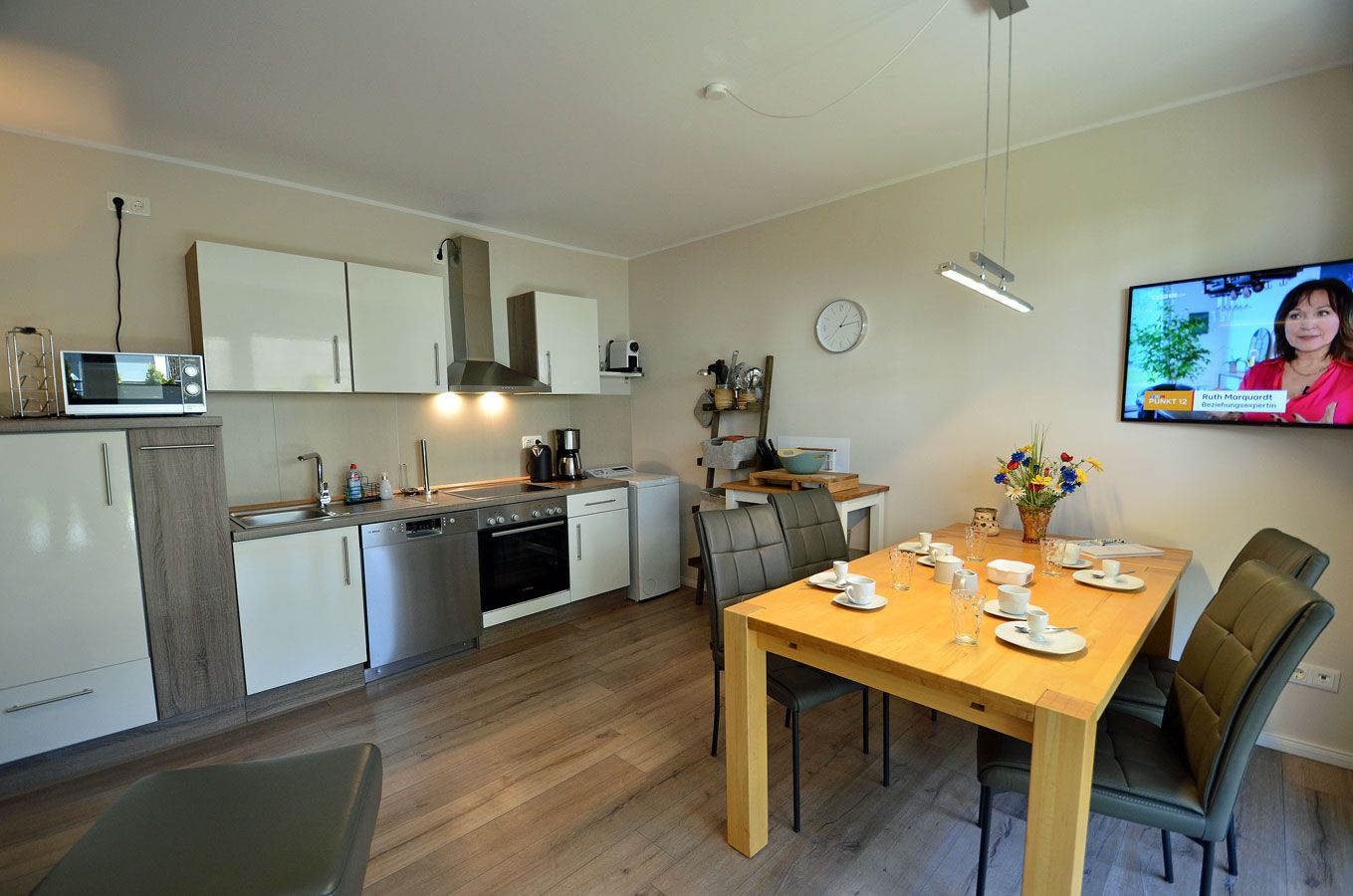 A modern kitchen with a dining area, including a wooden table set for four, a microwave, and a coffee maker.