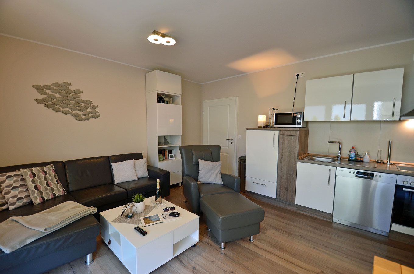 A compact living space with a sofa, armchair, coffee table, kitchenette, and a wall art piece.