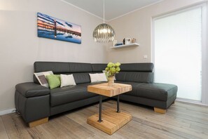 A modern living room with a sectional sofa, a wooden coffee table, a hanging pendant light, and a painting on the wall. - First floor, modern amenities, central location, about 200 m from the sandy beach (Baltic Sea) (Juliusruh)