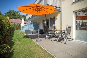 Eine Terrasse mit Gartenmöbeln, einem Tisch und einem Sonnenschirm.