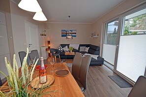 Una sala de estar moderna con zona de comedor, que incluye un sofá, una mesa dispuesta para dos personas y un ventanal grande.