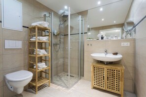 Ein modernes Badezimmer mit einer Duschkabine, Toilette, Waschbecken und einem Holzboden mit Handtüchern.
