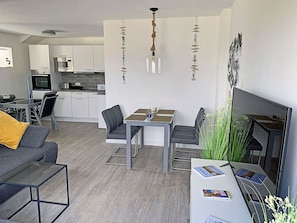 Ein modernes Wohnzimmer mit Essbereich, grauen Sofas, einem Couchtisch und einem Fernseher.