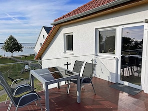 Ein Balkon mit Glastisch und Stühlen, ein weißes Gebäude mit rotem Dach und Blick auf das Wasser.