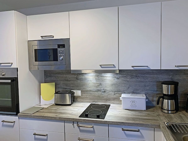 Eine moderne Küche mit weißen Schränken, einer eingebauten Mikrowelle, einem Toaster, einer Kaffeemaschine und einer Brokkasten.