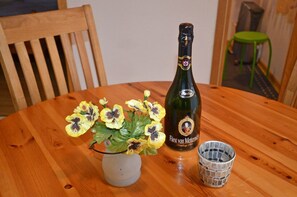 A wooden table with a bottle of champagne, a glass, and a vase with flowers. - Bungalow right on the sandy beach of the Baltic Sea, sleeps up to 4 people, with 2 bedrooms) (Juliusruh)