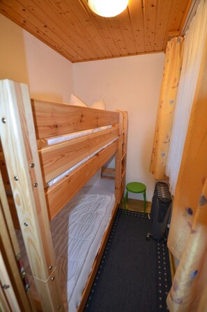 Ett litet, smalt rum med en våningssäng, en grön pall och en värmare.