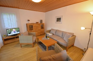 A cozy living room with a television, wicker furniture, a sofa, and a wooden cabinet. - Bungalow right on the sandy beach of the Baltic Sea, sleeps up to 4 people, with 2 bedrooms) (Juliusruh)