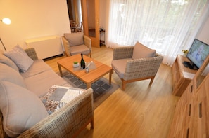 A cozy living room with a sofa, two wicker chairs, a coffee table with a bottle and glasses, a television, and a wooden cabinet. - Bungalow right on the sandy beach of the Baltic Sea, sleeps up to 4 people, with 2 bedrooms) (Juliusruh)