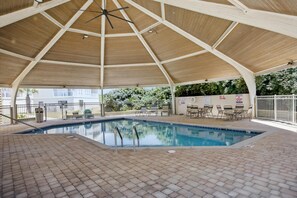 Ein überdachter Pool mit Holzboden, umgeben von Liegestühlen und einem weißen Zaun.