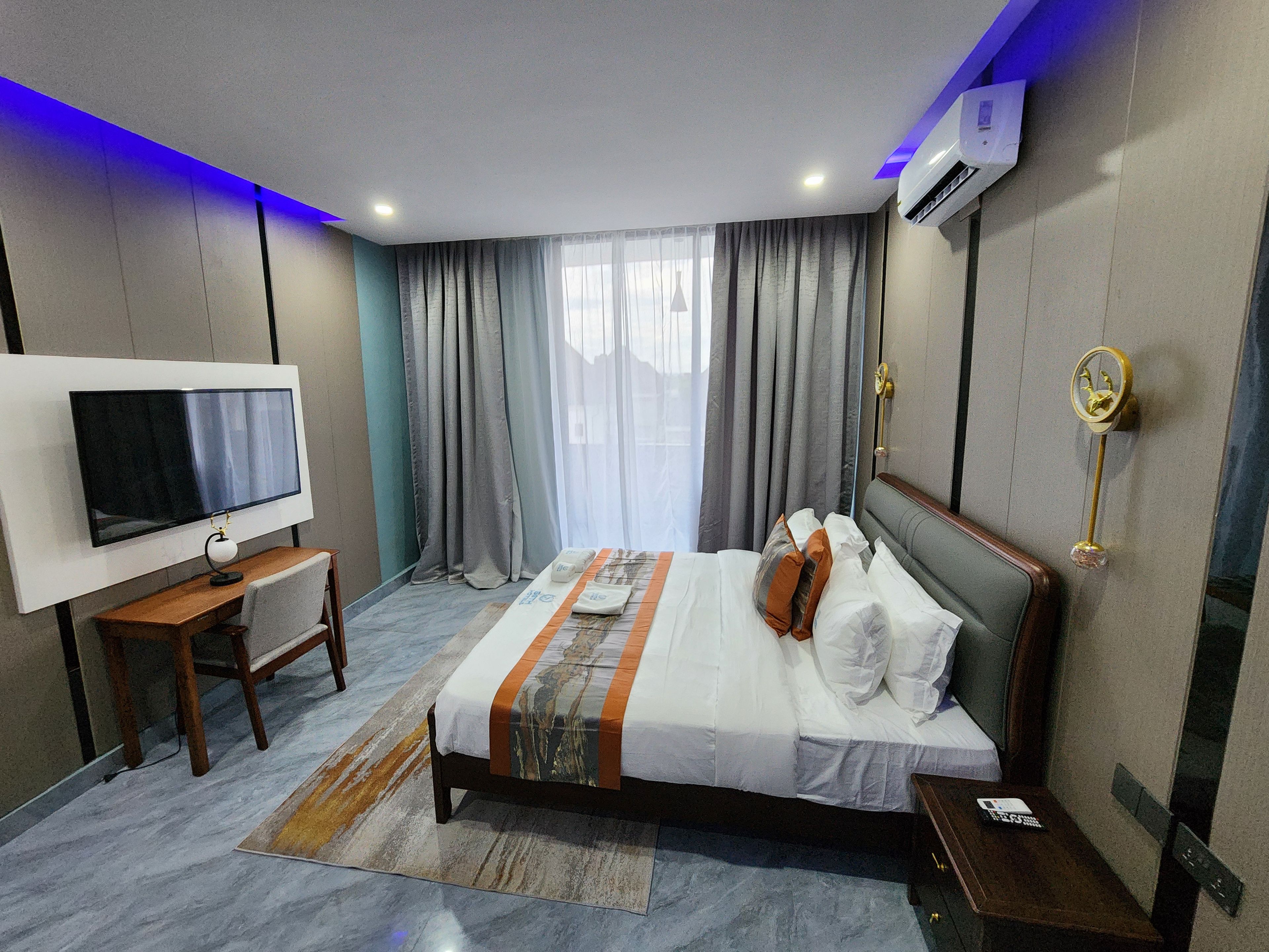 Una habitación de hotel con cama, televisor, escritorio y ventana con cortinas.