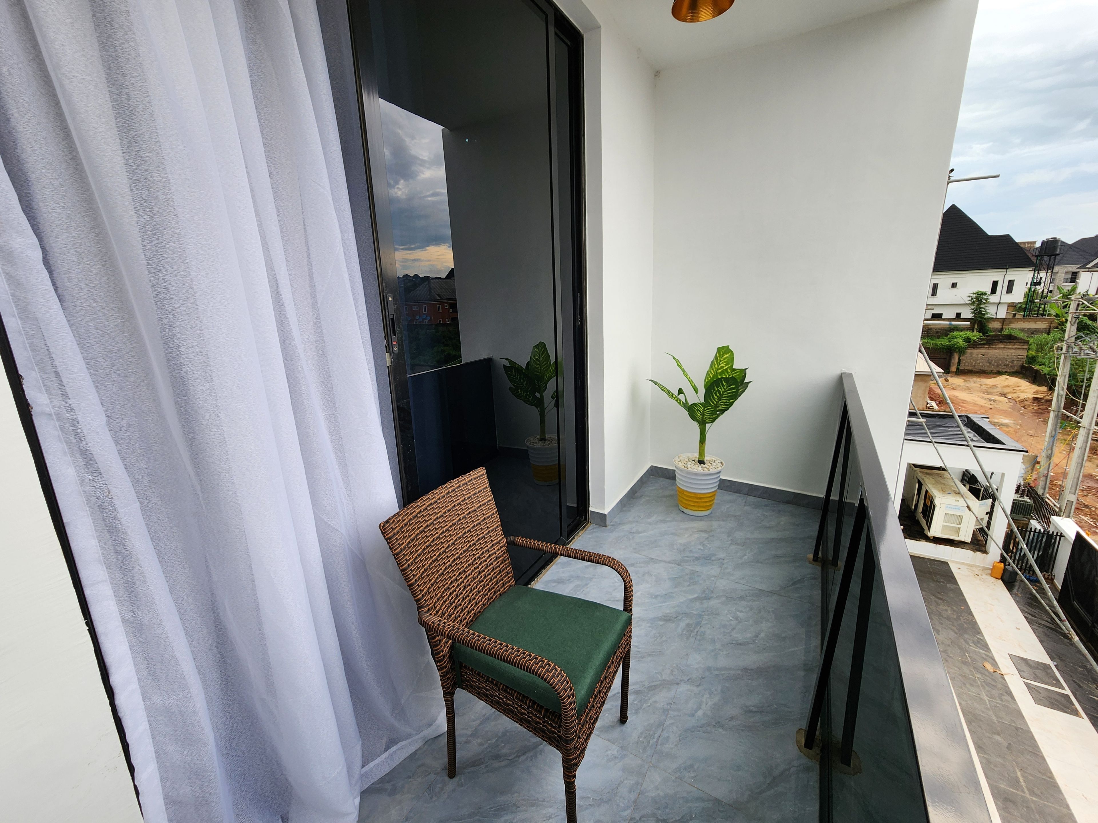 A balcony with a wicker chair, a potted plant, and a view of the surrounding area.